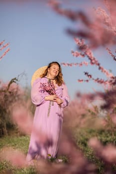 Woman blooming peach orchard. Against the backdrop of a picturesque peach orchard, a woman in a long pink dress and hat enjoys a peaceful walk in the park, surrounded by the beauty of nature