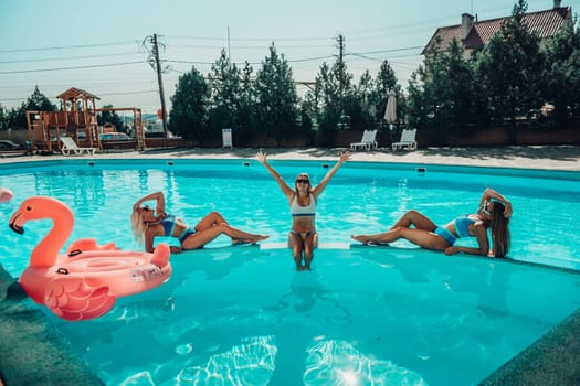 Three women are sitting in a pool, one of them is wearing a pink floatie. Scene is lighthearted and fun, as the women are enjoying their time together in the pool