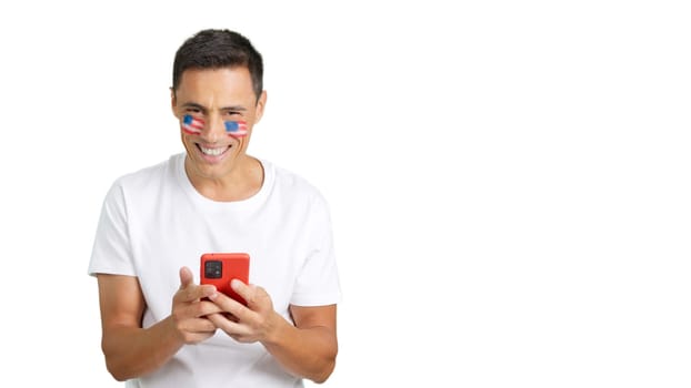 American man with the flag of United States painted on his face, looking at his mobile phone smiling