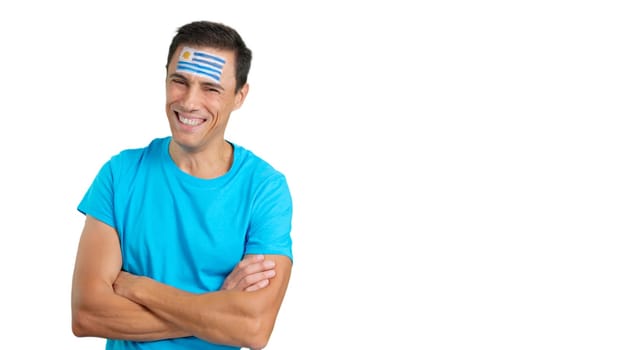 Man standing with uruguayan flag painted on face smiling with arms crossed