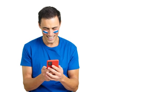 Thailand supporter with the flag of Thailand painted on his face, looking at his mobile phone smiling