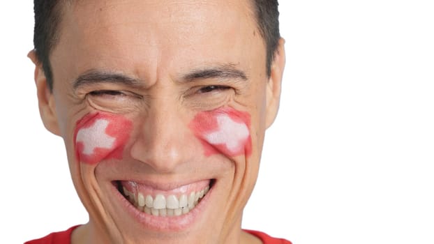 Close up of a man with a swiss flag painted on the face smiling at camera