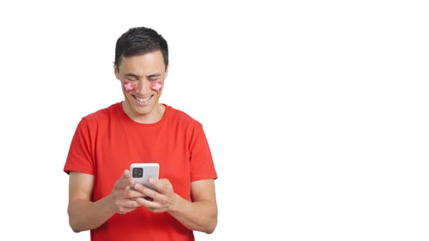 Swiss supporter with the flag of Switzerland painted on his face, looking at his mobile phone smiling