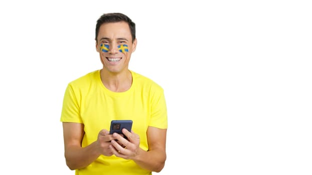 Swedish supporter with the flag of Sweden painted on his face, looking at his mobile phone smiling