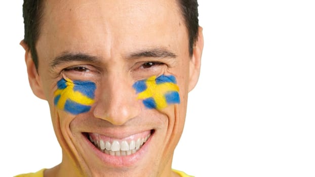 Close up of a caucasian man with a swedish flag painted on the face smiling at camera