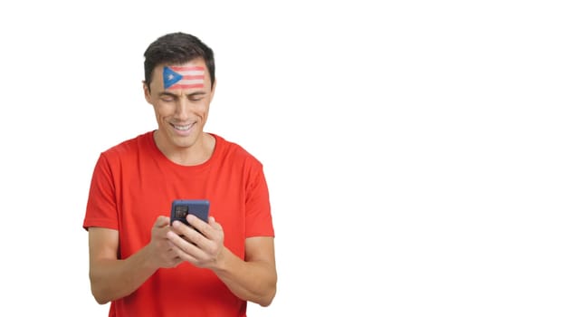 Puerto rican supporter with the flag of Puerto Rico painted on his face, looking at his mobile phone smiling