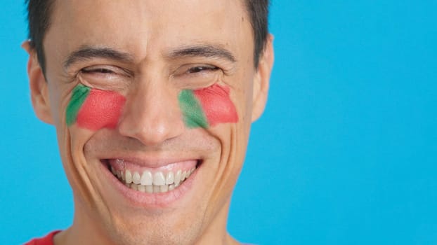 Close up of a man with a portuguese flag painted on the face smiling at camera