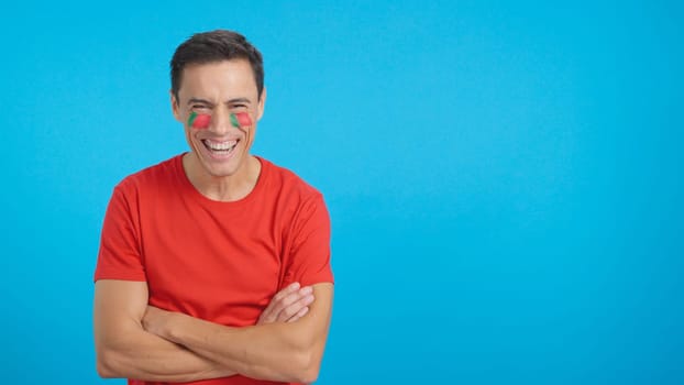 Man standing with portuguese flag painted on face smiling with arms crossed