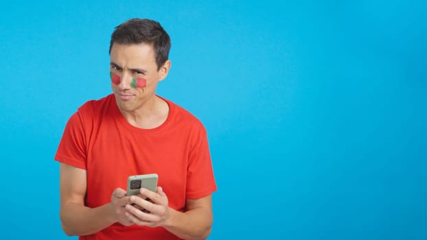 Portuguese supporter with the flag of Portugal painted on his face, looking at his mobile phone smiling