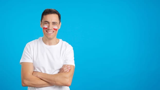 Man standing with polish flag painted on face smiling with arms crossed