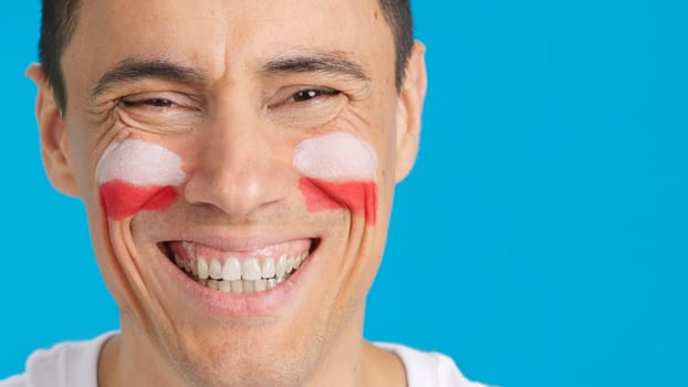 Close up of a man with a polish flag painted on the face smiling at camera