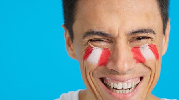 Close up of a man with a peruvian flag painted on the face smiling at camera