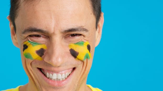 Close up of a man with a jamaican flag painted on the face smiling at camera