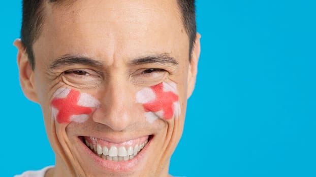 Close-up of a caucasian man with a english flag painted on the face smiling at camera