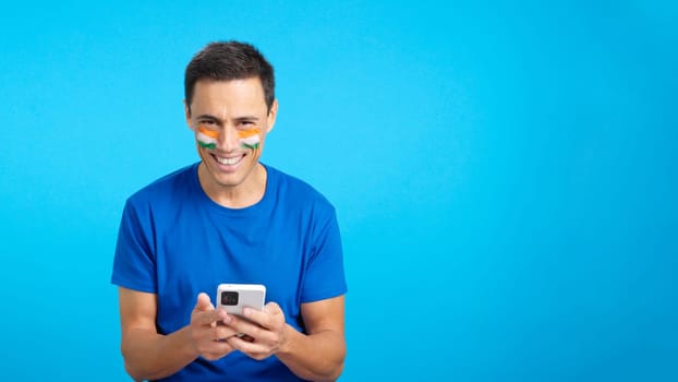Indian man with the flag of India painted on his face, looking at his mobile phone smiling