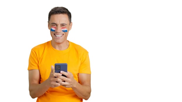 Dutch supporter with the flag of Holland painted on his face, looking at his mobile phone smiling
