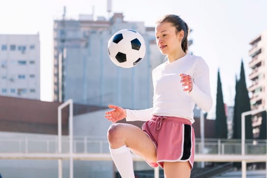female soccer player kicking the ball with her knee on an urban football court, concept of sport and active lifestyle