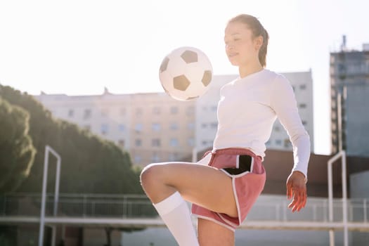 caucasian female soccer player kicking the ball with her knee on an urban football court, concept of sport and active lifestyle