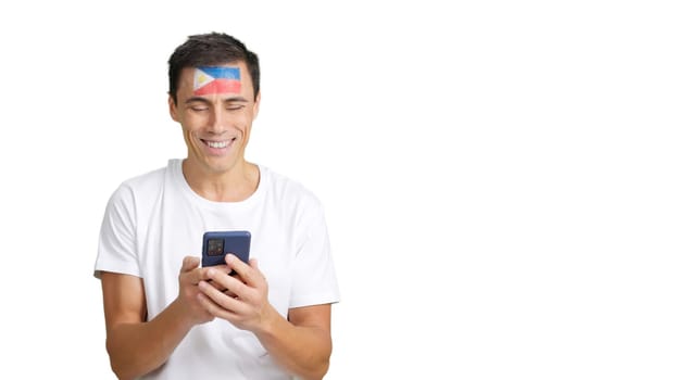 Philippines supporter with the flag of Philippines painted on his face, looking at his mobile phone smiling