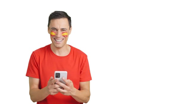 Spanish man with the flag of Spain painted on his face, looking at his mobile phone smiling