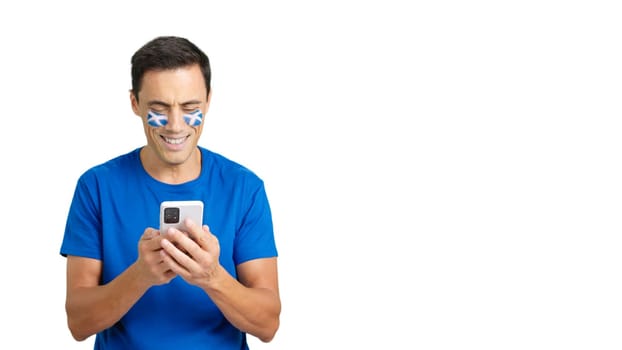 Scottish supporter with the flag of Scotland painted on his face, looking at his mobile phone smiling