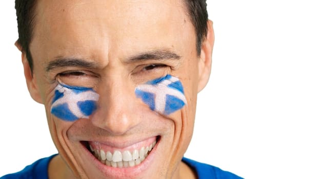 Close up of a man with a scottish flag painted on the face smiling at camera