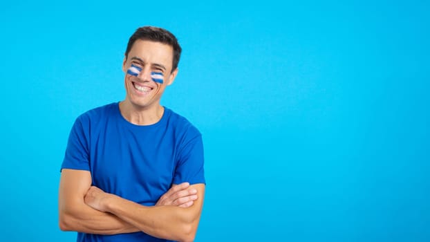 Man standing with salvadoran flag painted on face smiling with arms crossed