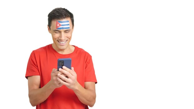 Cuban supporter with the flag of Cuba painted on his face, looking at his mobile phone smiling