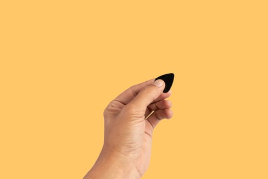 Black male hand holding a guitar pick isolated on yellow background. High quality photo