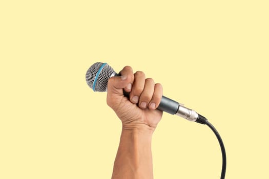 Black male hand holding a microphone isolated on light yellow background. High quality photo