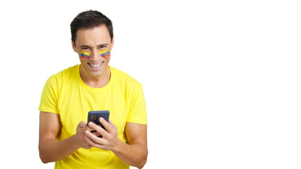 Colombian supporter with the flag of Colombia painted on his face, looking at his mobile phone smiling