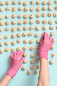 A chef's hands in a rubber glove carefully lays out semi-cooked raw dumplings on a blue background, top view.