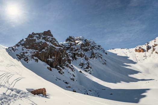 Alpine Serenity: Cold winter sunlight dances on three rocky peaks, creating mesmerizing shadows on the snow-covered mountain pass.