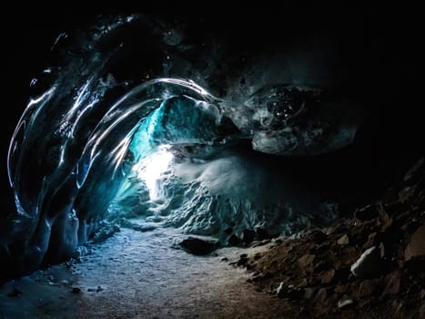 A mystical ice cave in the dark landscape emits a radiant electric blue light, resembling a midnight liquid wave, creating a mesmerizing art piece in the darkness.