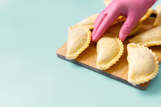A baker wearing a rubber glove arranges uncooked samosas on the table. These are frozen ready-to-cook traditional Central Asian delicacies, copy space.