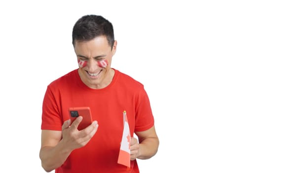 Canadian supporter with the flag of Canada painted on his face, looking at his mobile phone smiling