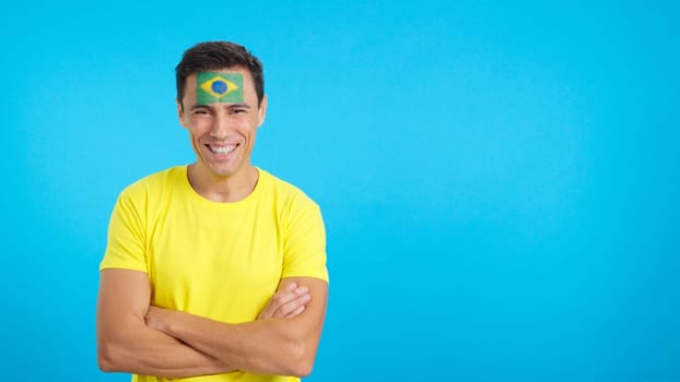 Man standing with brazilian flag painted on face smiling with arms crossed