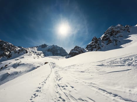 Amazing winter landscape of a frozen mountainside with the sun breaking through the clouds - a mountaineering trail winding through the snowy terrain.