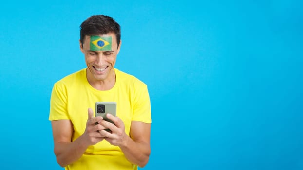 Brazilian man with the flag of Brazil painted on his face, looking at his mobile phone smiling