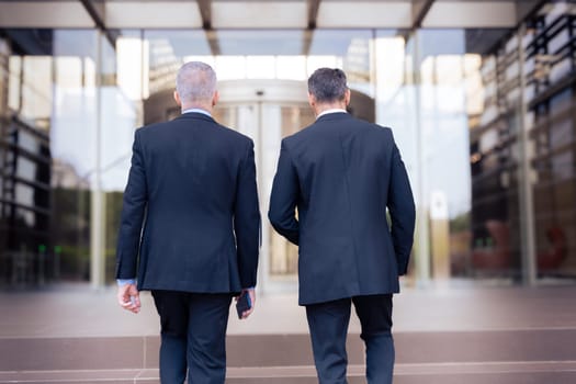 two caucasian male business colleagues talking happily, co-workers talking walking to enter the office building where they work