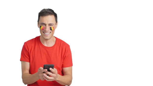 Belgian supporter with the flag of Belgium painted on his face, looking at his mobile phone smiling