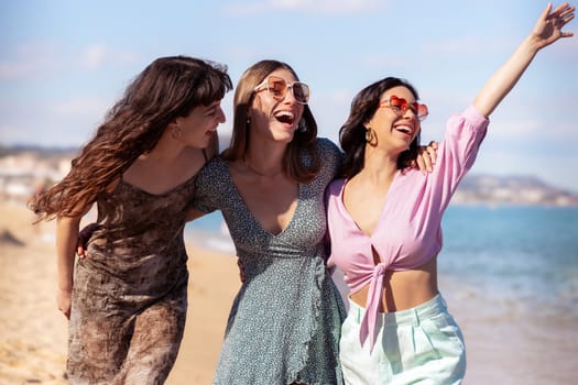 Cheerful multiethnic friends with sunglasses happy on vacation on the beach, looking at the camera.