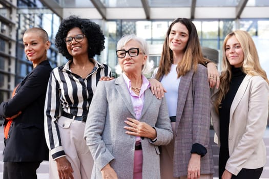 Five businesswomen standing side by side with their arms crossed looking at the camera happy. Suitable for team, friendship and diversity concepts.