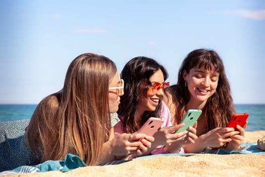 Group of smiling multiethnic women enjoying vacation. Beautiful and cheerful Gen Z girls with their mobile phones pose looking at the camera with a mobile phone.