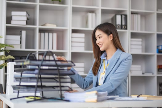 Young female accountant in a modern office, organizing documents and smiling, showcasing professionalism and efficiency.