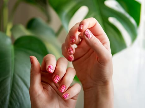 Aesthetic visual of two female hands with short nails with neon stamping manicure. Hand with stylish bright pink neon stamping nail art design manicure on green tropical monstera plant background