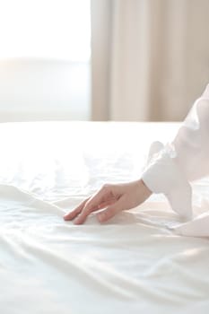 Woman Hand touching bed sheets, closeup. Young woman intimacy on bed. Soft, gentle, tender cozy morning concept