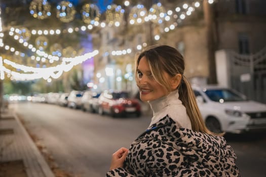 A woman wearing a leopard print jacket is smiling in front of a car. The scene is set in a city at night, with lights and cars visible in the background. The woman is enjoying her time