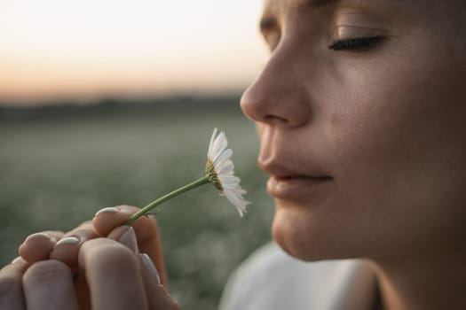 A woman is holding a flower and smelling it. Concept of calm and relaxation, as the woman takes a moment to appreciate the beauty of the flower