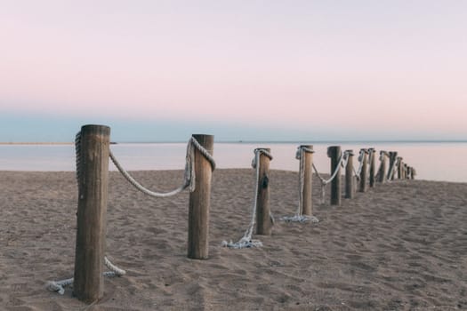 A row of wooden posts with rope tied to them on a beach. The beach is calm and peaceful, with the ocean in the background